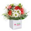 A scene of heartfelt celebration unfolds in this joyful bouquet, poised in a clean white gift bag that seems tailor-made for a stroll along Wanstead's charming high street. Coral and peach carnations, each petal tenderly ruffled and soft, mingle with lush red carnations to create a canvas of inviting warmth. Bright white daisies with golden-green centers are scattered throughout, capturing the cheerful spirit of local gardens and echoing the playful laughter of families in Wanstead Park. Wisps of pure white baby's breath add a featherlight touch, suggesting carefree innocence and gentle affection. Subtle hints of dusky purple buds peep out on one side, lending a whisper of freshness and newness to the ensemble. The entire bouquet is surrounded by a crown of deep green, glossy leaves-streamlined and verdant, like the tree-lined walks that criss-cross the neighbourhood. The arrangement's rounded, abundant form and thoughtfully matched textures are emphasised by the pure white background, focusing all attention on its vibrant palette and graceful lines. The handles of the gift bag arch invitingly above, making it easy for a special surprise to travel from a Wanstead florist's doorstep directly to someone's home. This bouquet is more than an arrangement-it's a sincere gesture, crafted to mark a birthday, congratulate an achievement, or simply share the radiance of fresh flowers with a neighbour, friend, or loved one in the Wanstead area.